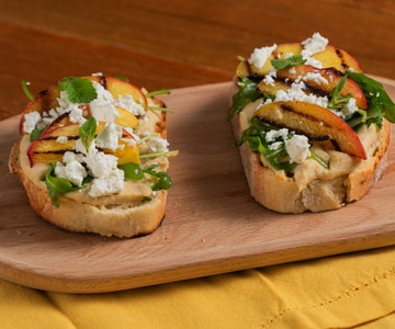 Crostini with hummus, grilled peaches, feta, and arugula