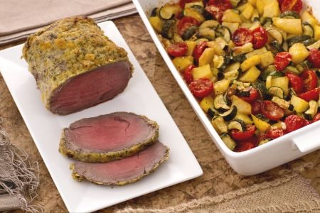 Roast beef with citrus fruits with a tray of potatoes, zucchini, and cherry tomatoes