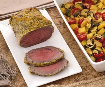 Roast beef with citrus fruits with a tray of potatoes, zucchini, and cherry tomatoes